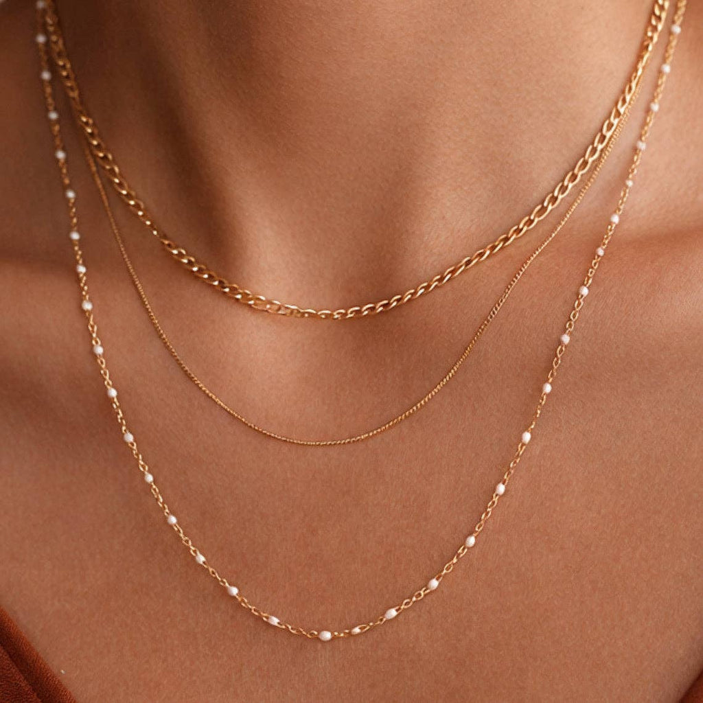 Two gold necklaces with small beads on a person's neck