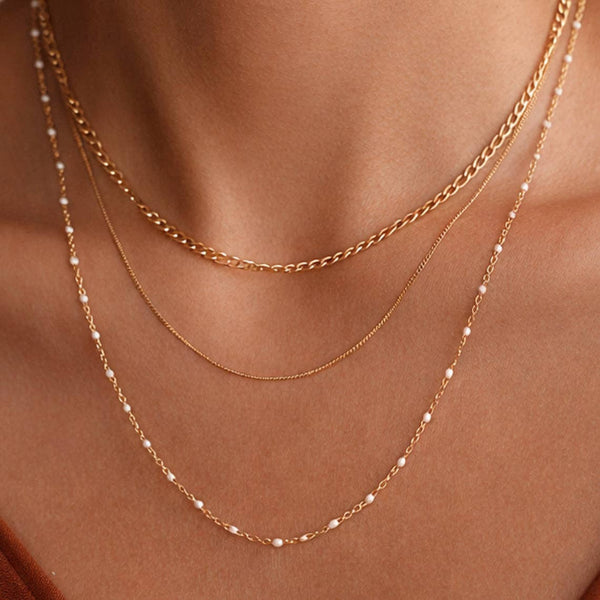 Two gold necklaces with small beads on a person's neck