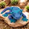 Blue rubber toy lizard on a rock with plants in the background