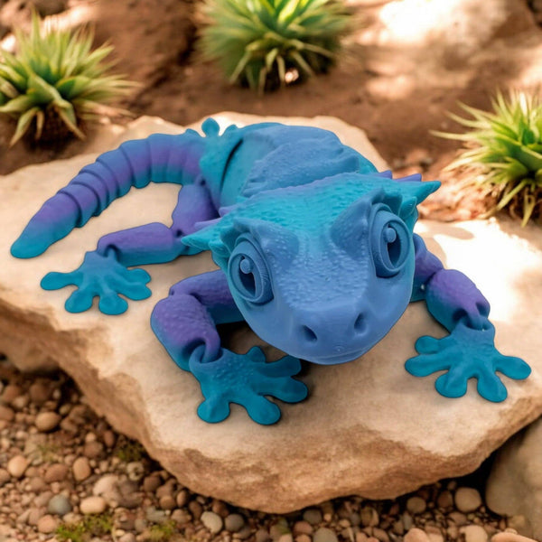 Blue rubber toy lizard on a rock with plants in the background