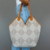 Person holding a patterned tote bag with brown handles against a gray background