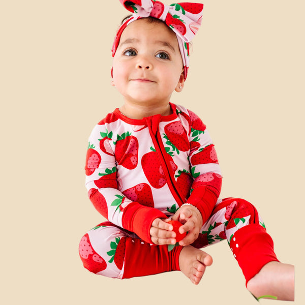 Baby wearing a strawberry-themed outfit with a matching headband on a white background