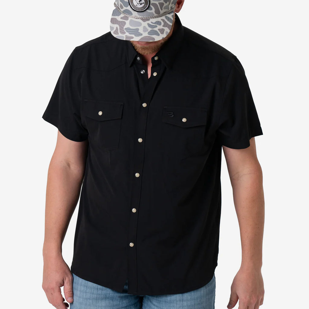 Person wearing a black short-sleeve button-up shirt with light blue jeans on a white background