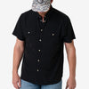 Person wearing a black short-sleeve button-up shirt with light blue jeans on a white background