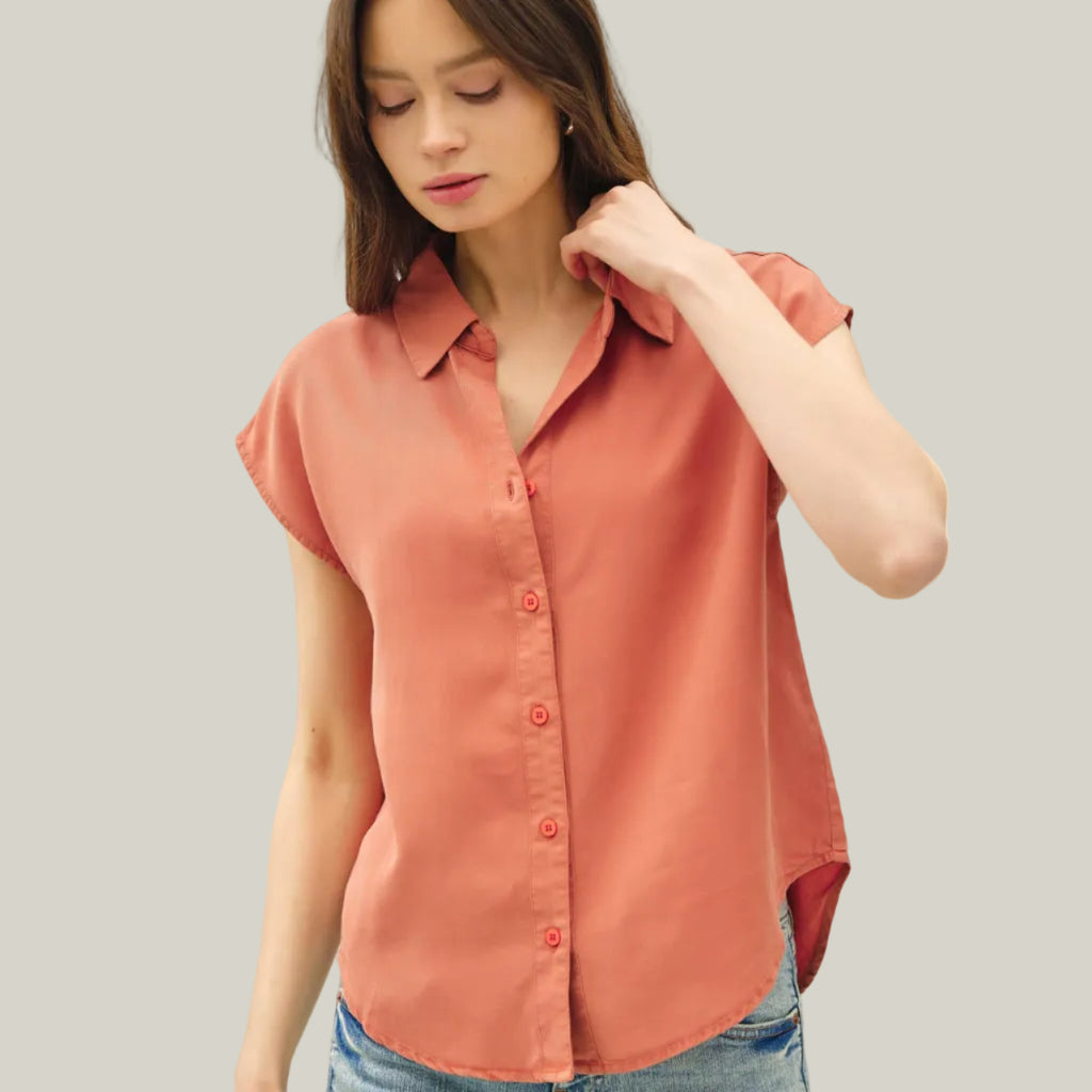Woman wearing a coral button-up shirt and blue jeans on a white background