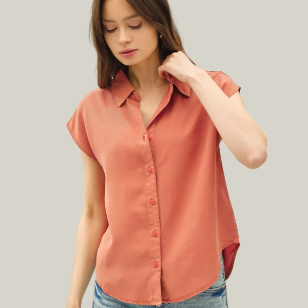 Woman wearing a coral button-up shirt and blue jeans on a white background