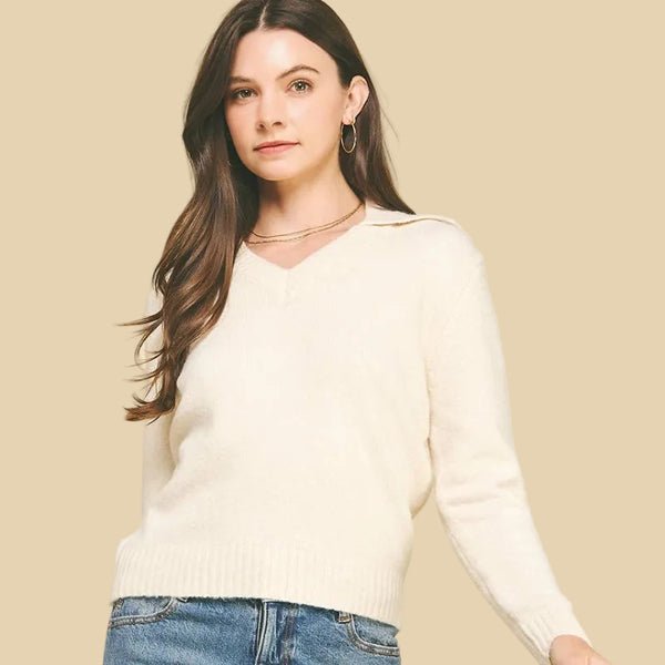 Woman wearing a cream sweater and blue jeans against a beige background