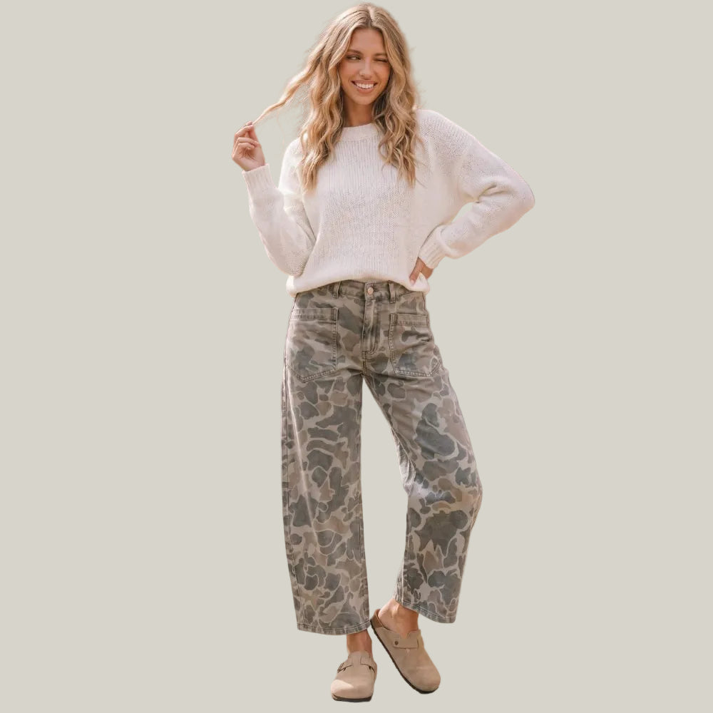 A woman stands outdoors wearing a cream knit sweater, high-waisted wide-leg camouflage pants, and beige clogs.