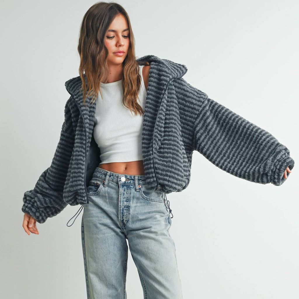Woman wearing a gray oversized sweater, white crop top, and light blue jeans against a plain background