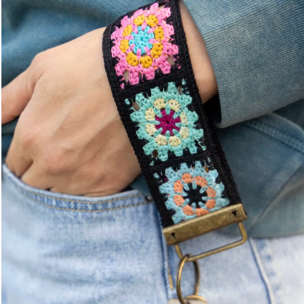 Colorful crocheted strap with floral patterns worn on a wrist, attached to a keychain.