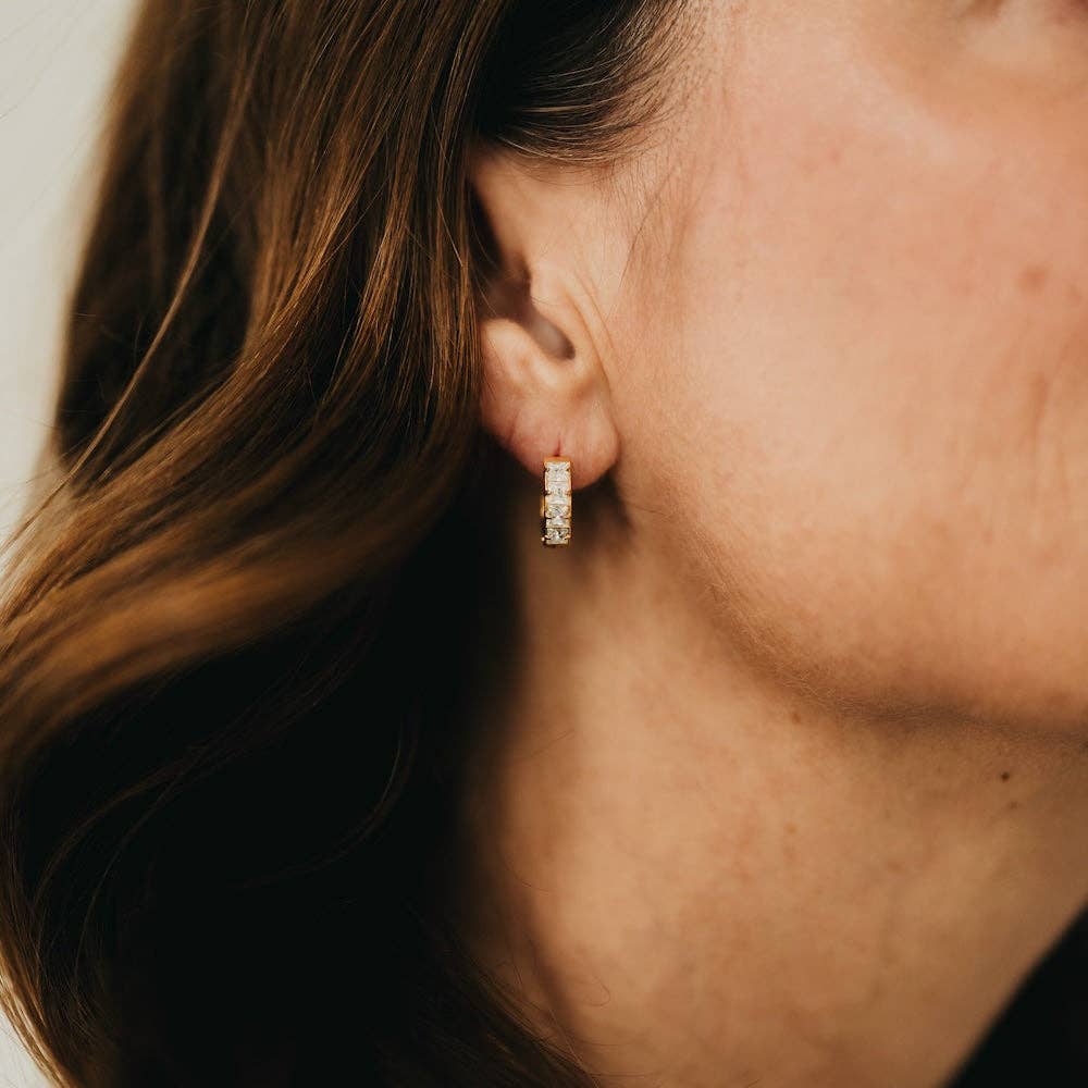 Close-up of an ear wearing a diamond earring with blurred hair and skin in the foreground
