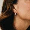 Close-up of an ear wearing a diamond earring with blurred hair and skin in the foreground