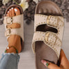 Brown sandals with gold buckles held by a hand, with another sandal on a foot in the background.
