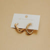 Gold hoop earrings on a white card against a beige background