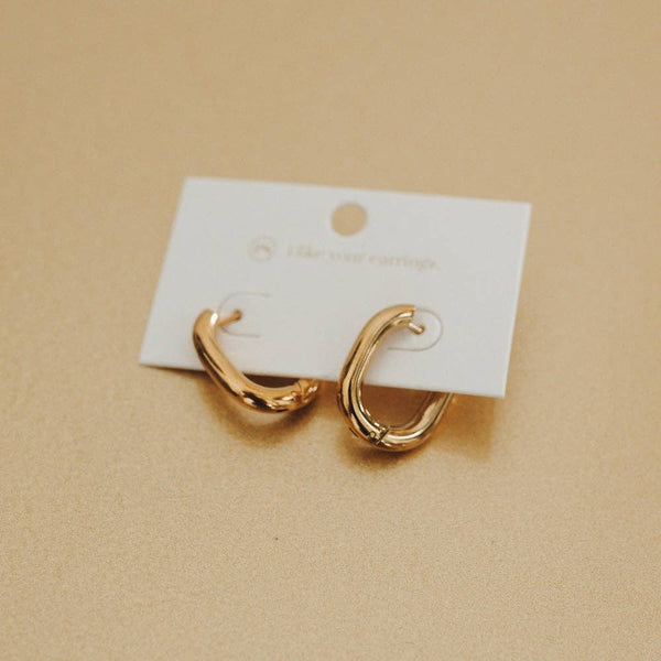 Gold hoop earrings on a white card against a beige background