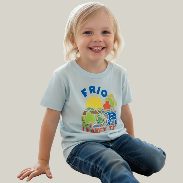 Child wearing a light blue t-shirt with colorful graphics and text, sitting on a wooden floor.