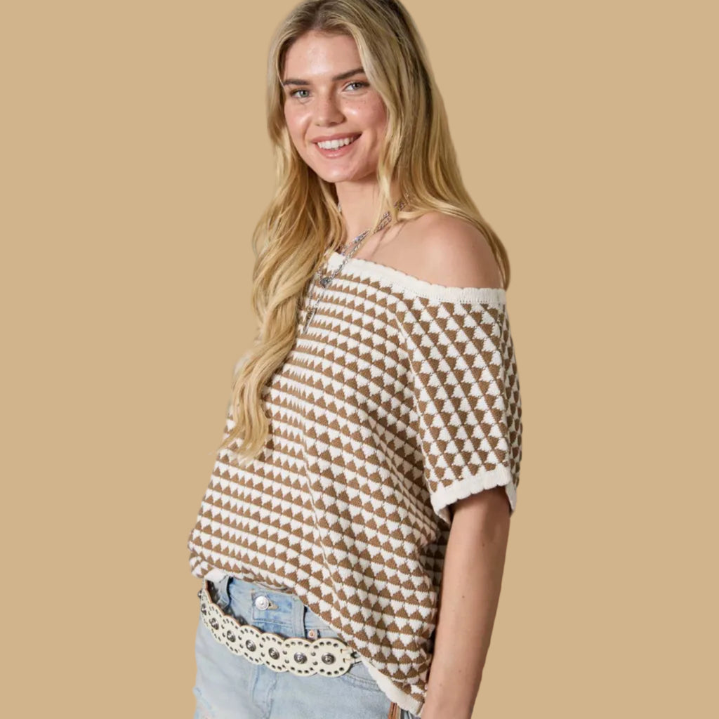 Woman wearing a patterned top and denim shorts standing against a textured wall.