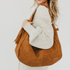 Person holding a brown leather handbag with a white sweater