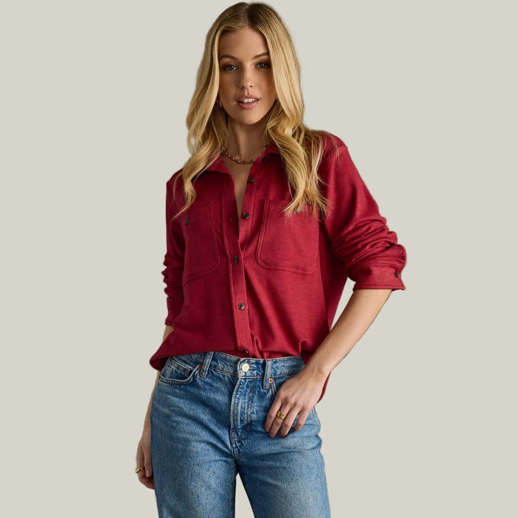 Woman wearing a red shirt and blue jeans against a gray background
