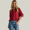 Woman wearing a red shirt and blue jeans against a gray background