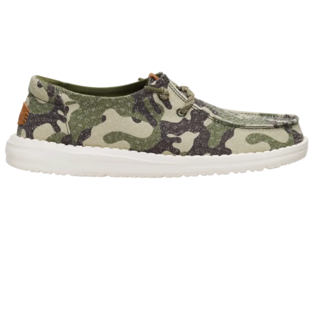A single casual boat shoe with a green, beige, and black camouflage pattern canvas upper, a white rubber sole, and metal eyelets, shown in profile against a light off-white background.