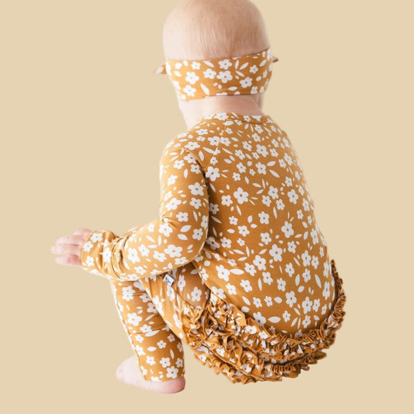 Baby wearing a mustard yellow floral outfit on a white background