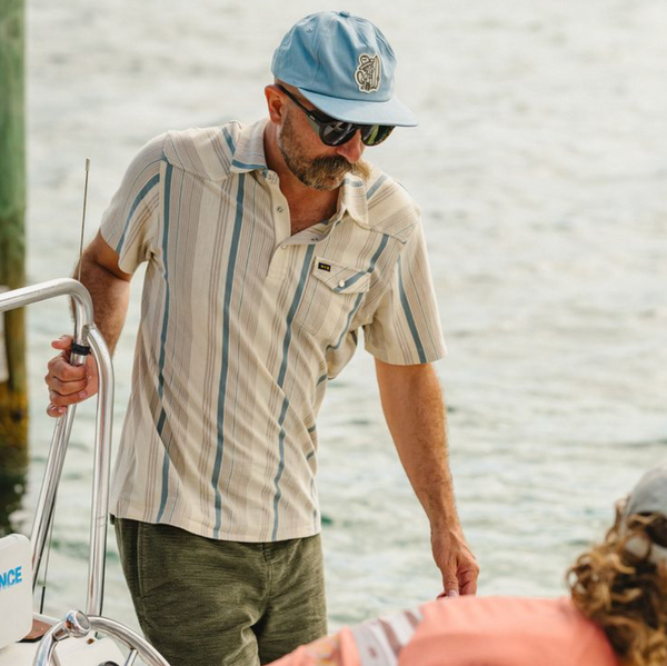 Man on a boat wearing a striped shirt and cap, with water in the background