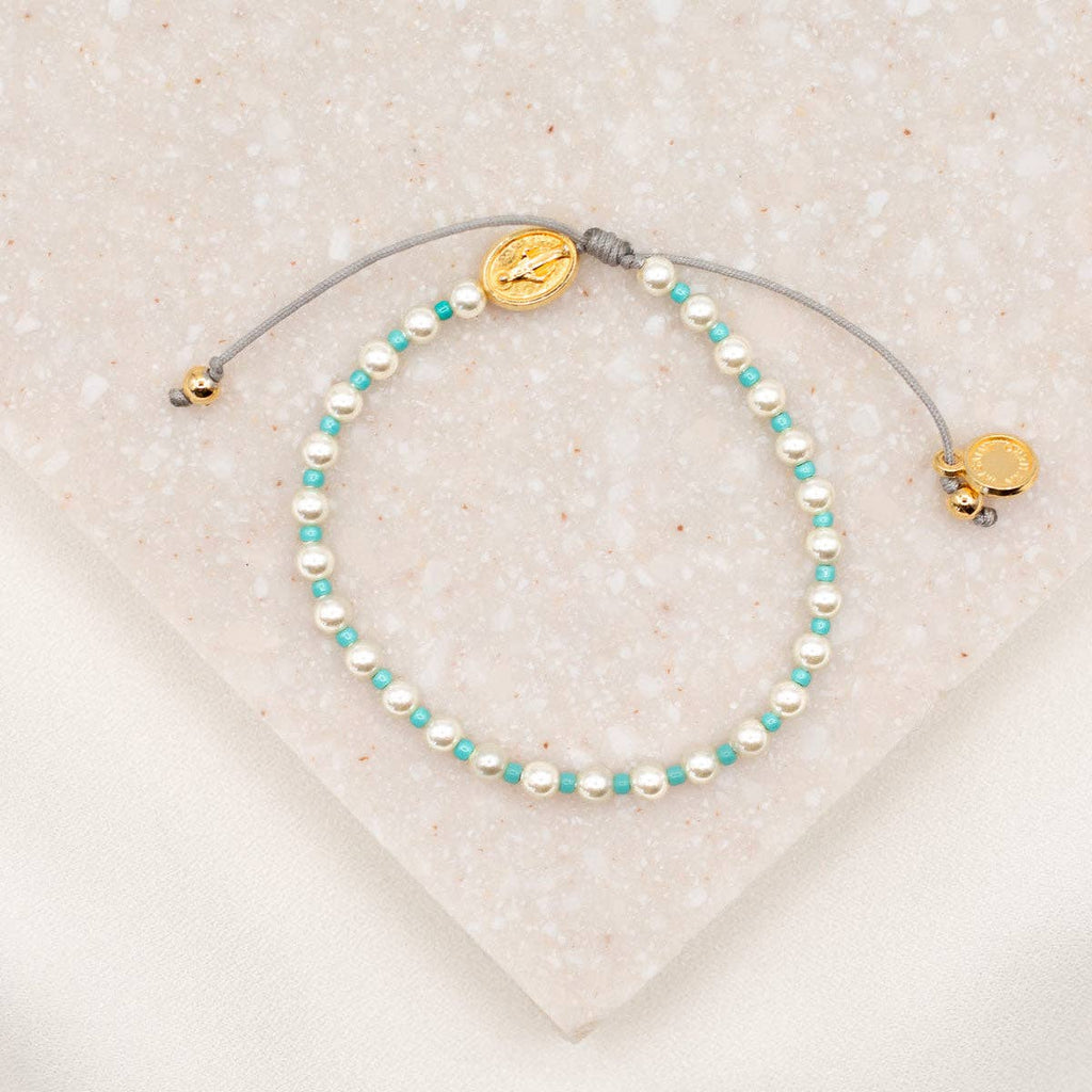Pearl and turquoise beaded bracelet with gold accents on a textured beige surface