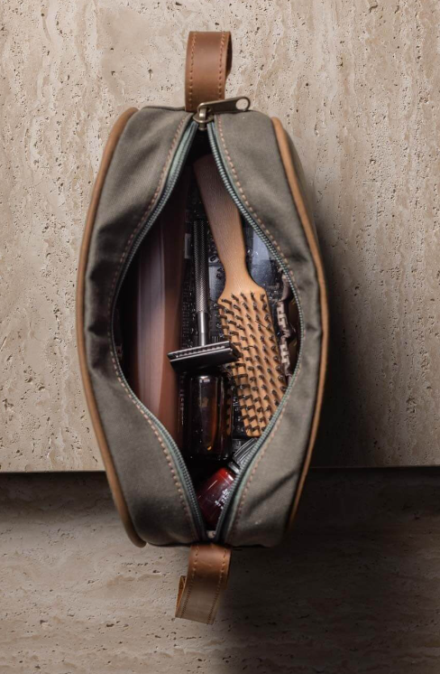 Open toiletry bag with grooming items against a textured wall