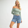 Woman wearing a green off-shoulder top and denim shorts on a white background