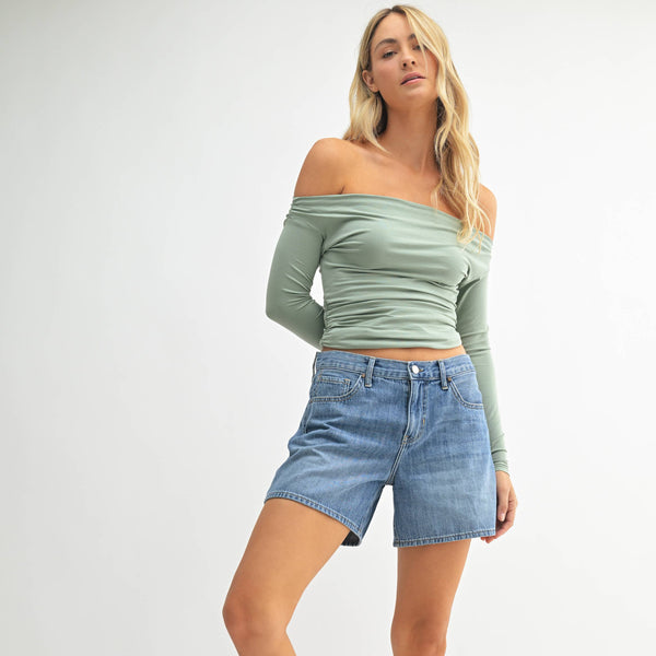 Woman wearing a green off-shoulder top and denim shorts on a white background