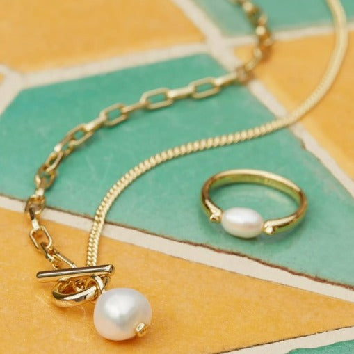 Gold necklace with pearl pendant  on a colorful geometric background