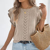 Woman wearing a beige knit top and denim shorts, holding a woven bag.