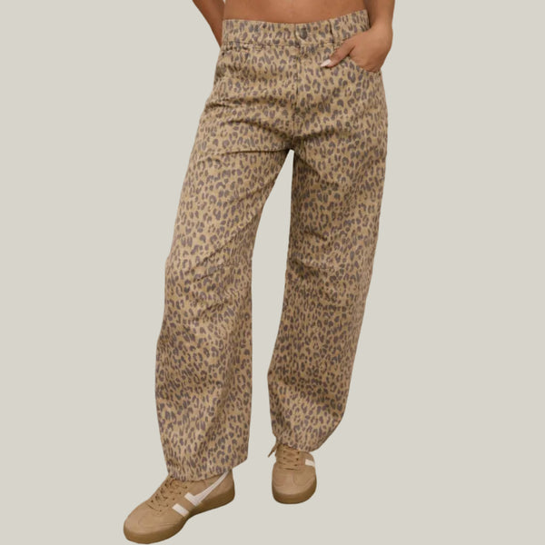 A person wearing loose, wide-leg leopard-print pants with a beige and brown animal pattern, paired with tan sneakers, standing  against a neutral background
