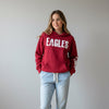 A red pullover hoodie displayed on a mannequin in a clothing store. The hoodie features the word 'EAGLES' in large distressed white letters across the chest and 'LEAKEY' printed vertically in white down one sleeve