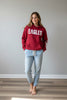 A red pullover hoodie displayed on a mannequin in a clothing store. The hoodie features the word 'EAGLES' in large distressed white letters across the chest and 'LEAKEY' printed vertically in white down one sleeve