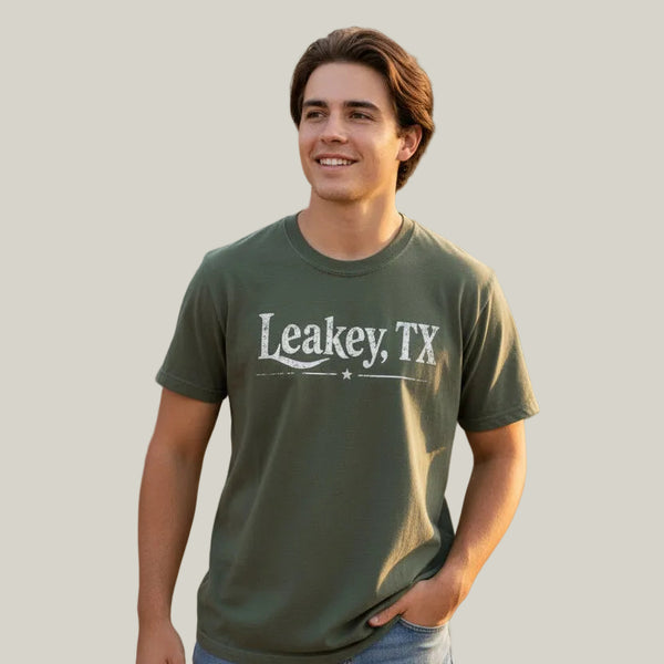 An olive green t-shirt on a model, featuring the text 'Leakey, TX' in a distressed white font across the chest.