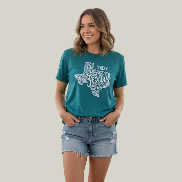 A teal short-sleeve graphic T-shirt hanging on a wooden hanger, featuring a white line-art Texas outline with the words 'LEAKY Texas' across the front.