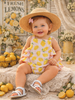 Child wearing a lemon-patterned outfit and straw hat in a lemon-themed setting.