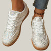 White sneakers with animal print pattern worn with rolled-up jeans on a neutral surface.