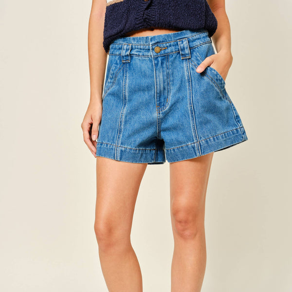 Person wearing blue denim shorts and brown loafers on a plain background