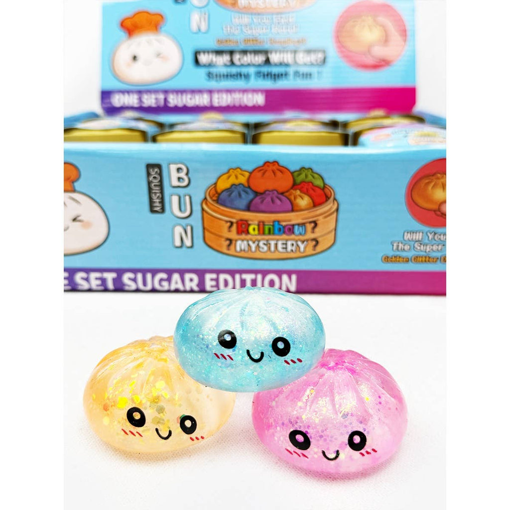 Three colorful bun-shaped squishies in front of a box labeled 'Rainbow Mystery' with a sugar edition theme.