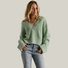 Woman wearing a light green knitted cardigan and blue jeans against a gray background