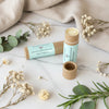 Two lip balm tubes with natural packaging on a marble surface with flowers and leaves.
