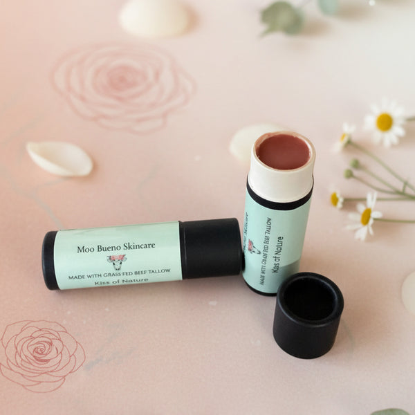 Two lip balm sticks with a black cap on a pink surface with floral elements.
