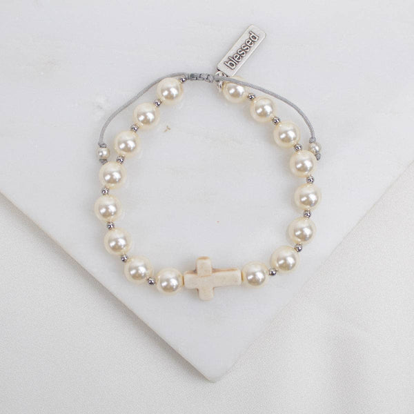 Pearl bracelet with a cross charm on a white background