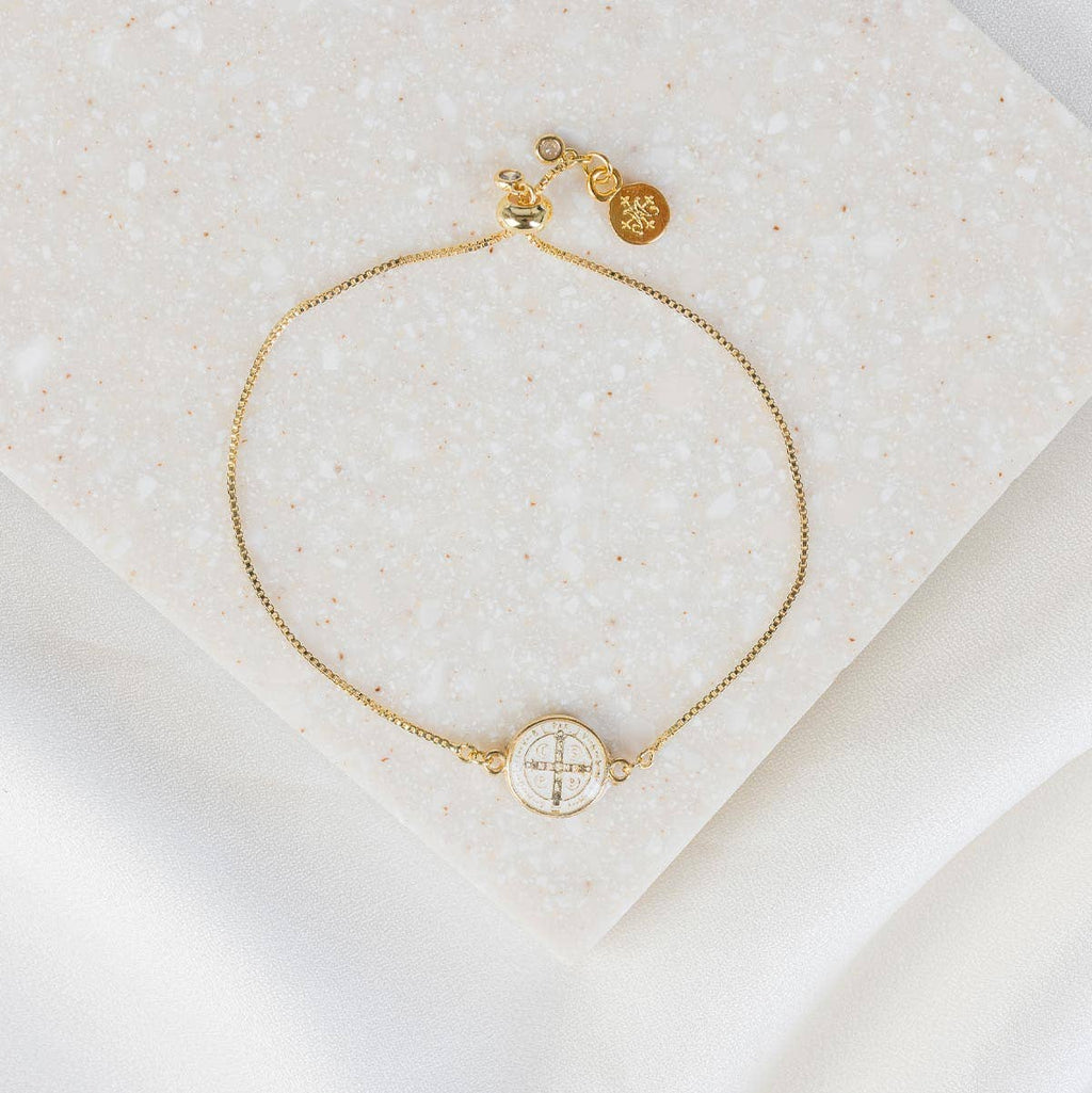 Gold bracelet with circular charm on a textured beige surface