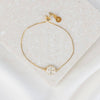 Gold bracelet with circular charm on a textured beige surface