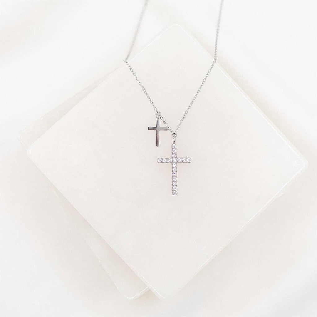 Two cross necklaces on a white textured surface
