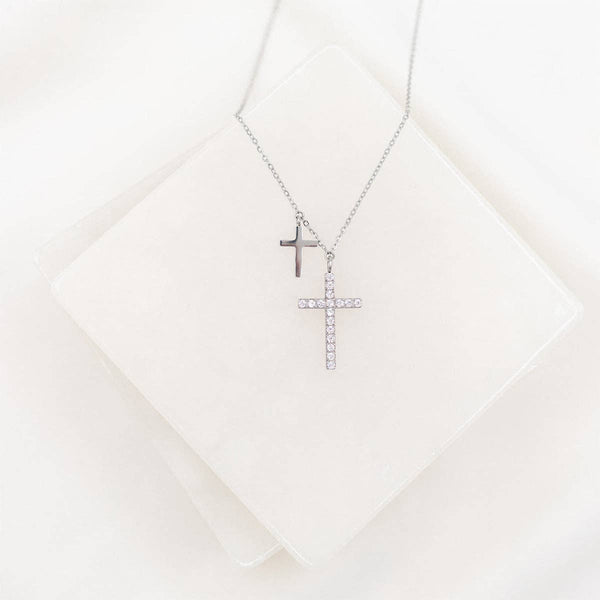 Two cross necklaces on a white textured surface